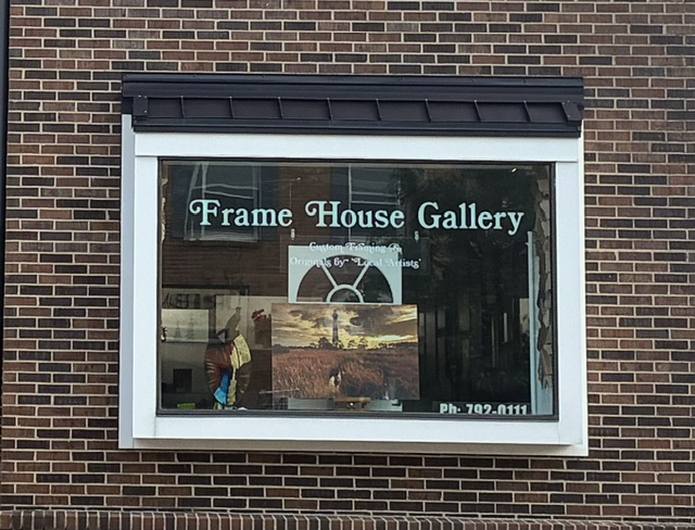 The gallery's display window set in the brick storefront, showing framed prints inside