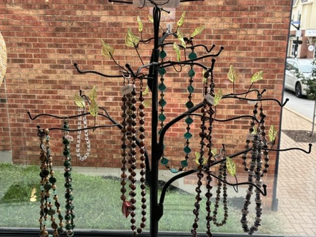 Beaded necklaces hanging from a wrought-iron jewelry tree in the window