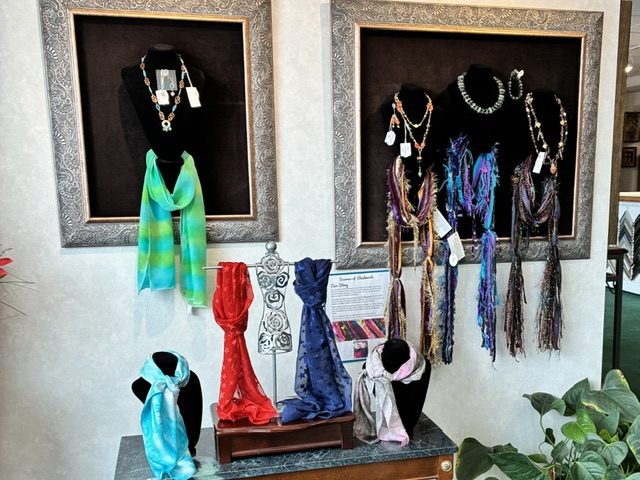 Silk scarves and beaded scarf necklaces in framed shadow boxes above a marble console