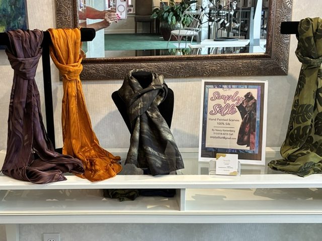 Hand-painted silk scarves in plum, amber and olive draped over display bars